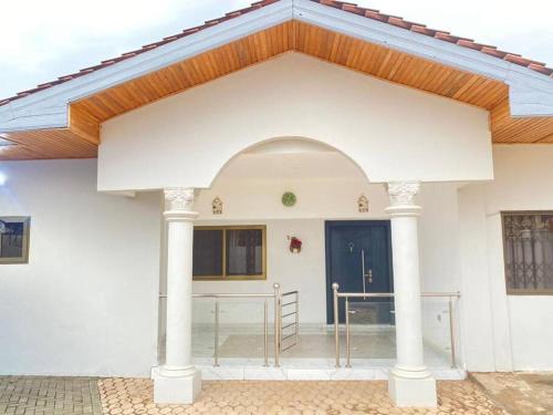 ein weißes Haus mit einem Holzdach und einer blauen Tür in der Unterkunft Executive Home away from Home in Accra