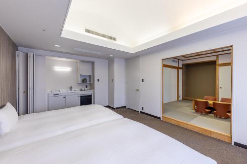 a bedroom with a large white bed and a kitchen at Court Hotel Asahikawa in Asahikawa