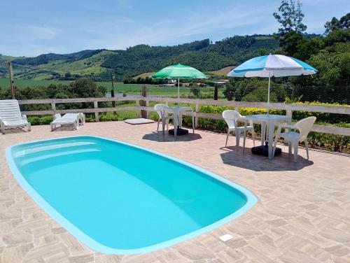 una piscina con tavolo, sedie e ombrelloni di Chácara do vô Meireles a Serra Negra