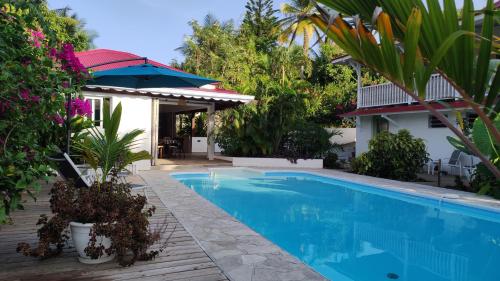 a swimming pool with an umbrella next to a house at Les Coulirooms - Gîte in Sainte-Anne