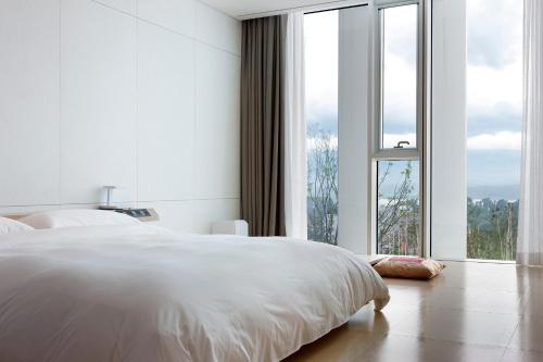 a white bedroom with a bed and a large window at SEAMARQ HOTEL in Gangneung