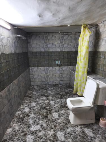 a dirty bathroom with a toilet and a yellow shower curtain at Mousa's studio in Jerash