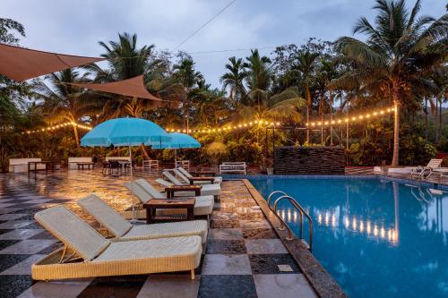 a pool with lounge chairs and umbrellas next to a resort at Wild Berry Resort Agonda in Canacona