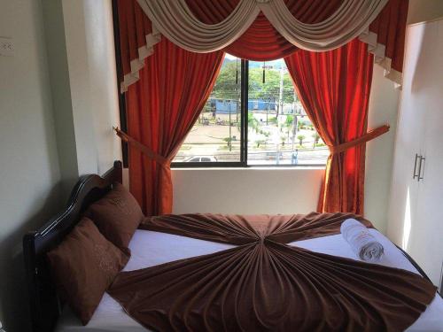 a bed in front of a window with red curtains at Hotel Shekinah Internacional in Esmeraldas
