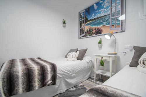 Dormitorio blanco con 2 camas y lámpara en Apartamento Arco de los Blanco, en Cádiz