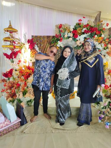 un grupo de tres mujeres parados frente a una pared floral en hotel lake town resort., en Kuala Kangsar