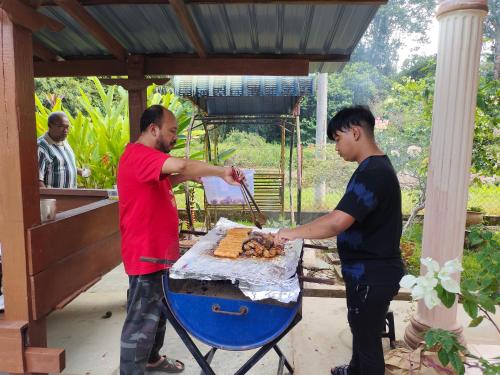 two men are cooking food on a grill at hotel lake town resort. in Kuala Kangsar