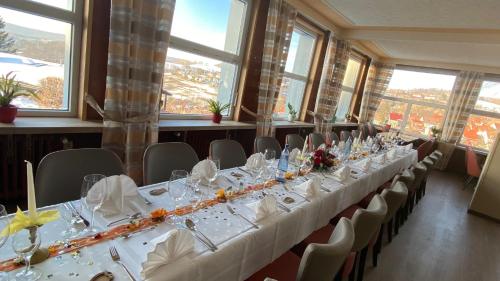 a long table with white tables and chairs in a room with windows at Berghotel Glockenberg in Sankt Andreasberg