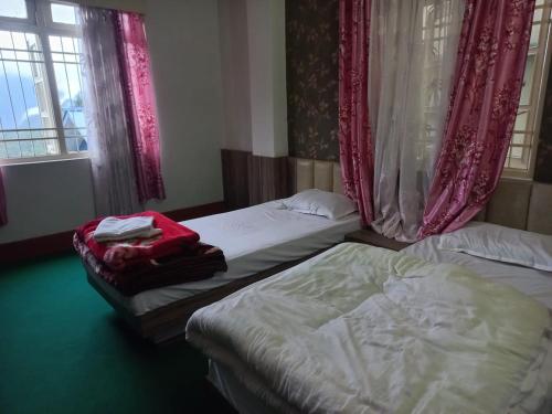 two twin beds in a room with red curtains at Mangan Stone Pebbles Lodge in Mangan