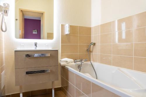 een badkamer met een bad, een wastafel en een spiegel bij Le Bon Cap in Plurien