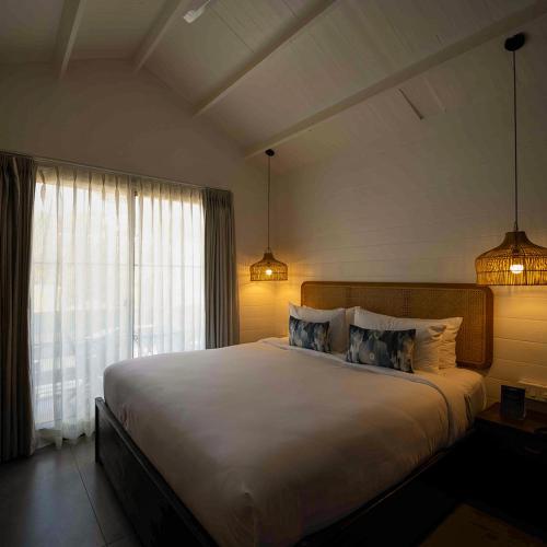 a bedroom with a large white bed with two lamps at Azora by Ayatana, Goa in Morjim