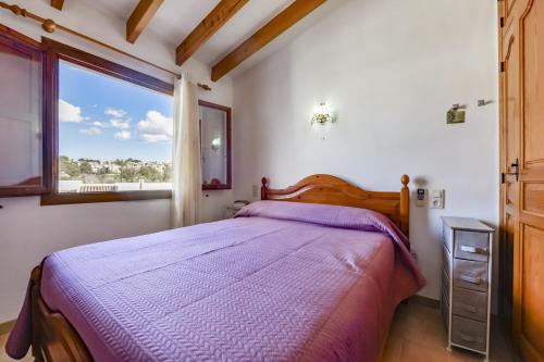 a bedroom with a bed with a purple comforter and a window at Rafol - Casa adosada con piscina comunitaria y tenis comunitario in Calpe