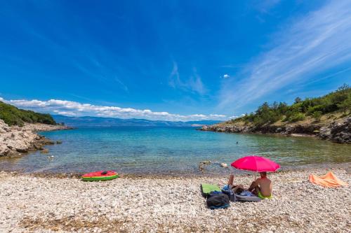 a woman sitting under a pink umbrella on a beach at House CAPRI with heated pool and sea view in Klimno