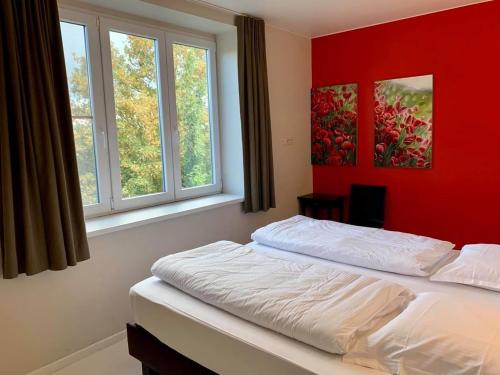 een slaapkamer met een bed met een rode muur en 2 ramen bij vakantiewoning het vijverhuis in Zillebeke