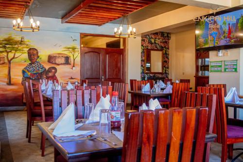 restauracja ze stołami i krzesłami oraz kobieta stojąca w tle w obiekcie Enkipai Hill Hotel w mieście Narok