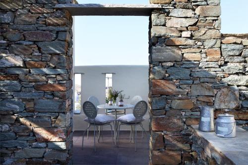 comedor con pared de piedra, mesa y sillas en Diles & Rinies, en Tinos