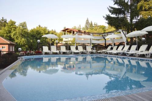 a swimming pool with white chairs and umbrellas at Spa Hotel Kleptuza in Velingrad