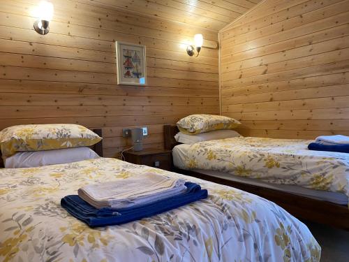 two beds in a room with wooden walls at Hazel Lodge luxury log cabin in South Wingfield