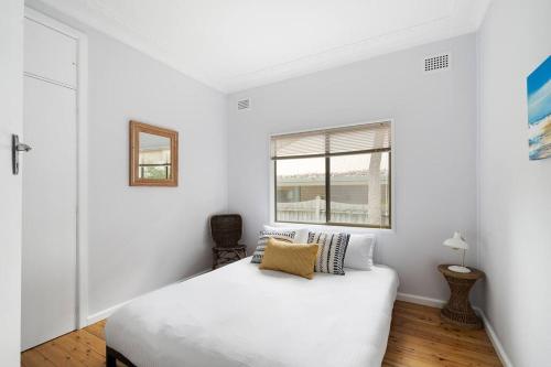 a white bedroom with a bed and a window at Pearl Beach House - 2 min to sand & sea - 2 semis in Pearl Beach