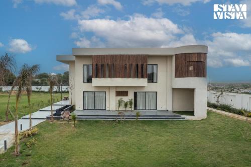 a house with a grassy yard in front of it at StayVista's The Sweet Life - 5BHK Farm-View Pet-Friendly Villa with Outdoor Pool in Sohna