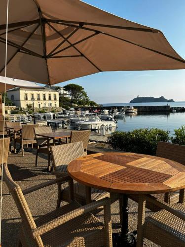 une table et des chaises en bois avec un parasol à côté d'un port de plaisance dans l'établissement Hôtel Restaurant Petra Cinta, à Barcaggio