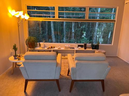 ein Wohnzimmer mit 2 Stühlen, einem Tisch und einem großen Fenster in der Unterkunft Casa Ócio By Canela do Mato in Palomas