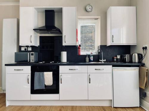 cocina con armarios blancos y fogones negros en Bright, spacious apartment with off-road parking en Bath