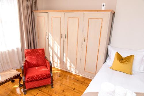 um quarto com uma cama e uma cadeira vermelha em Herberg Manor em Somerset East