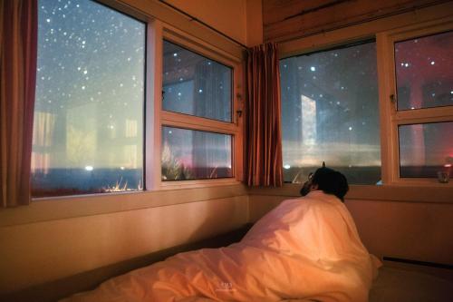 une personne dormant dans un lit sous une couverture donnant sur la fenêtre dans l'établissement The Lighthouse Cabin, à Borre