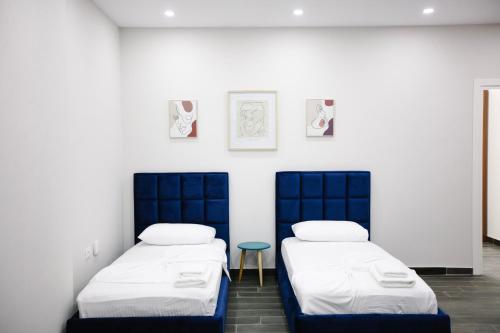 two beds in a white room with a stool between them at Andor Luxury Hotel & Duplex in Durrës