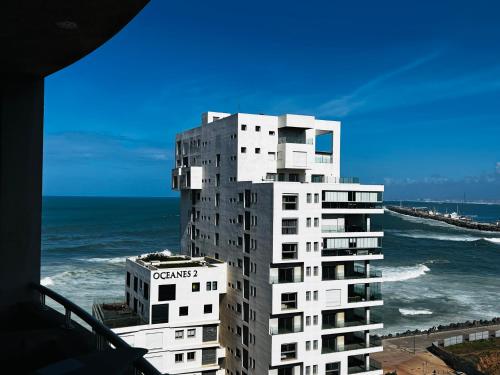 un grand bâtiment blanc à côté de l'océan dans l'établissement Magnifique appartement pleine vue mer Marina Casablanca, à Casablanca