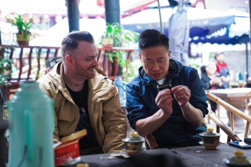 two men sitting at a table looking at something at Chengdu Local Tea Hostel - Short Walk To Taikooli - Chill & Social Coffee Lounge - Metro downstairs - Free Activities - Friendly English Speaking Staff - Tibet, Panda, Buddha & Snow Mountain Tours in Chengdu
