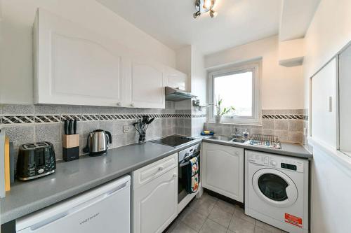 cocina con armarios blancos, lavadora y secadora en No 15 Brompton cross, en Londres