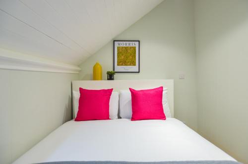 1 dormitorio con cama blanca y almohadas rosas en Split Level Studio at West Hampstead by Concept Apartments en Londres