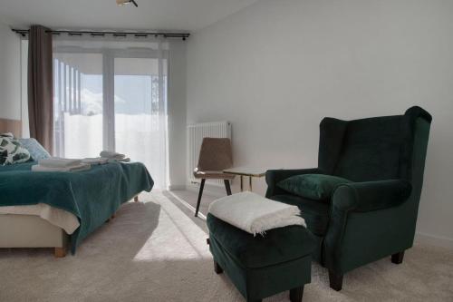 a bedroom with a bed and a green chair and a chair at Apartament Premium PINEA 302 in Pobierowo