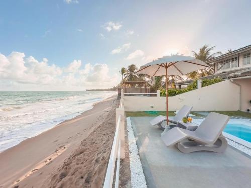 a pool with two chairs and an umbrella on the beach at Casa Sol Ipioca in Maceió