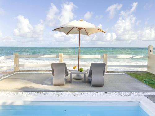 a table and chairs with an umbrella and the ocean at Casas Wave in Maceió
