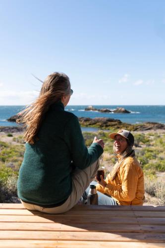 a man and a woman sitting on a bench near the ocean at Isla Leones Camps in Camarones