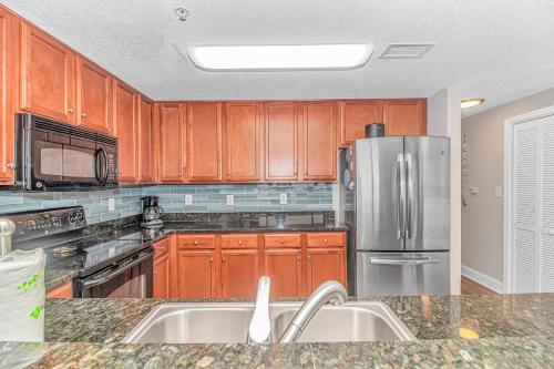 a kitchen with wooden cabinets and a stainless steel refrigerator at Stunning Double Balcony- Oceanfront 2 Bedroom, 2 Bath- Anderson Ocean Club 905 in Myrtle Beach