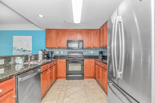 a kitchen with wooden cabinets and a stainless steel refrigerator at Stunning Double Balcony- Oceanfront 2 Bedroom, 2 Bath- Anderson Ocean Club 905 in Myrtle Beach