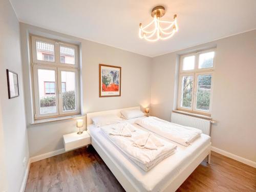 a bedroom with a large white bed with two windows at Hochwertig einger. Fewo mit Sonnenterrasse, Veranda, in Strandnähe in Kühlungsborn