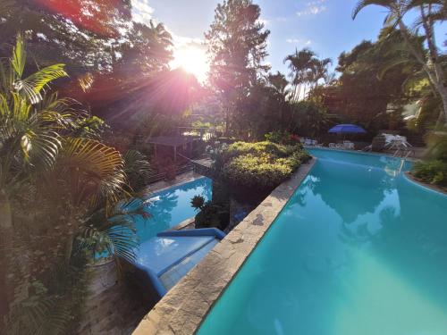a swimming pool in a garden with the sun setting at Pousada Baixa Verde in Triunfo
