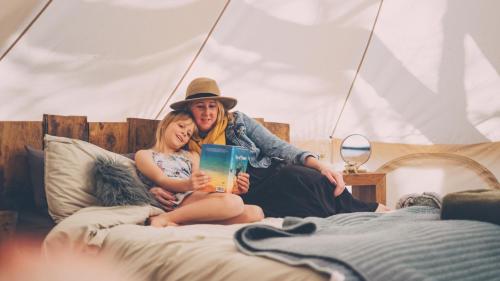 a man and woman sitting on a bed with a book at Cuddfan Bach (The Little Hideaway) at Camp Plas in Welshpool
