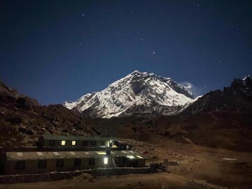 une montagne enneigée la nuit avec un bâtiment devant dans l'établissement Sherpa Lodge, à Lobujya