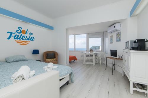 a bedroom with a bed and a kitchen and a table at Apartamento Sol da Falésia in Sesimbra