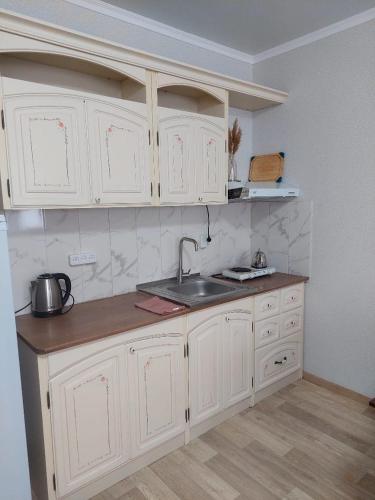 una cocina con armarios blancos y fregadero en Абажур, en Aktobe