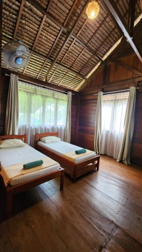 two beds in a room with wooden floors and windows at UKCC Hotel in Kota Bawah Timur