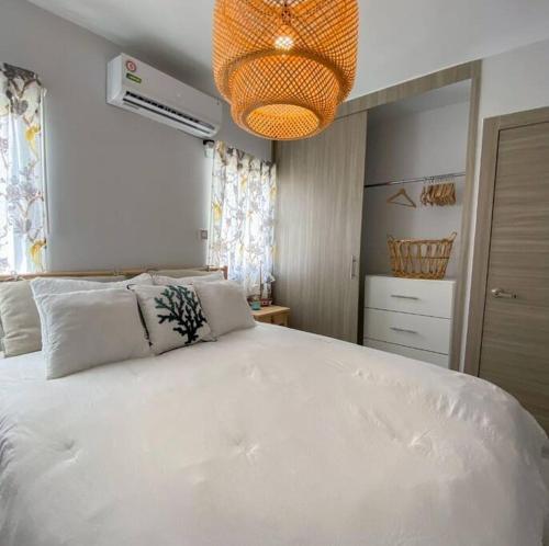 um quarto com uma grande cama branca e um lustre em Relaxing condo near airport PUJ Pool/Wi-fi em Punta Cana
