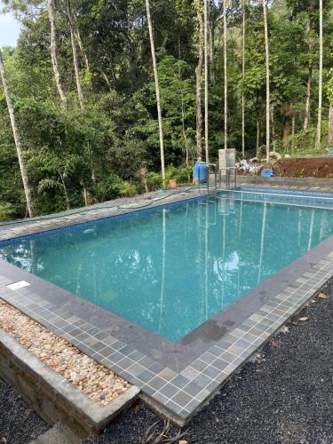 a swimming pool with turquoise blue water and trees at Wetlands Wayanad Resort with Natural Waterfalls in Padinjarathara