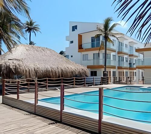 una piscina con sombrilla de paja y un edificio en HERMOSOS APARTAMENTOS FRENTE AL MAR EN EL CONDOMINIO PALMAR DE LOS VIENTOS, en San Bernardo del Viento